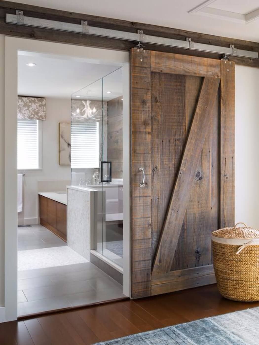 Wooden sliding barn door open to a bright bathroom with a glass shower and white vanity