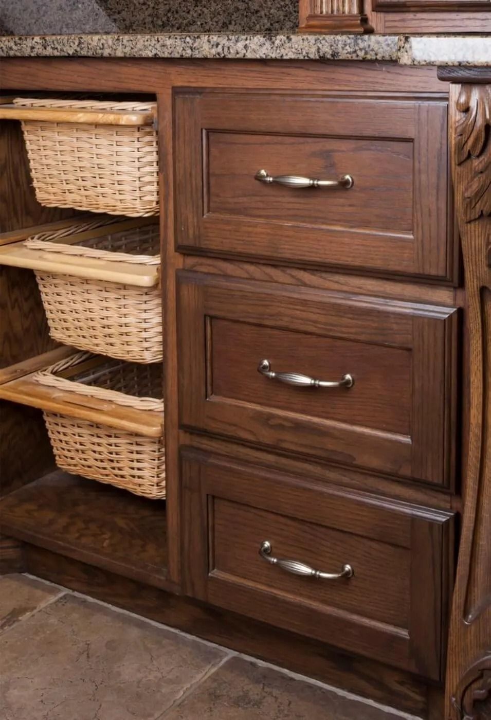 Wooden kitchen cabinet with three drawers and woven basket shelves beside a tiled floor