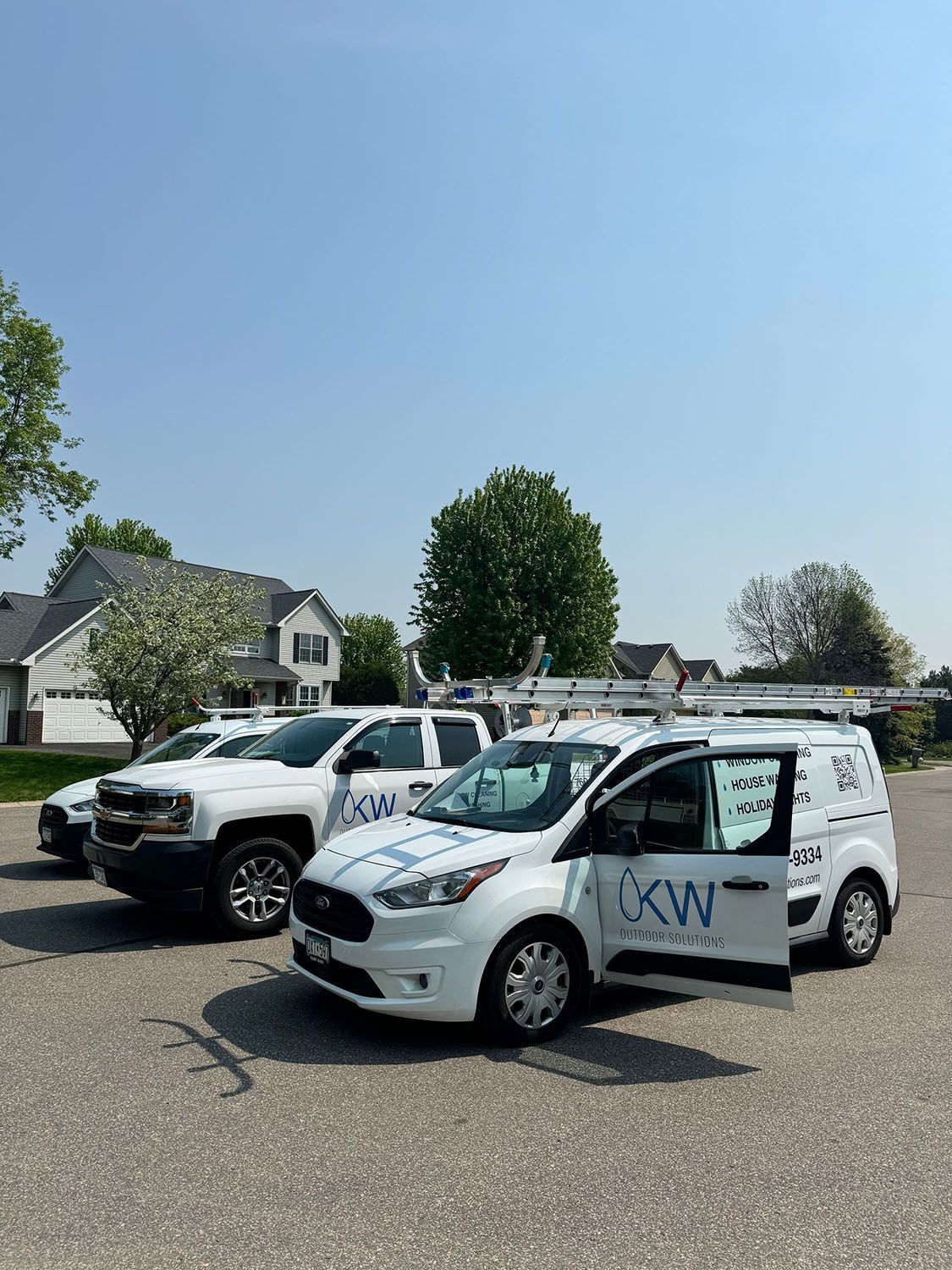 A row of white trucks and vans are parked in a parking lot.