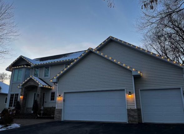 A large house with Christmas lights on the roof and garage doors.