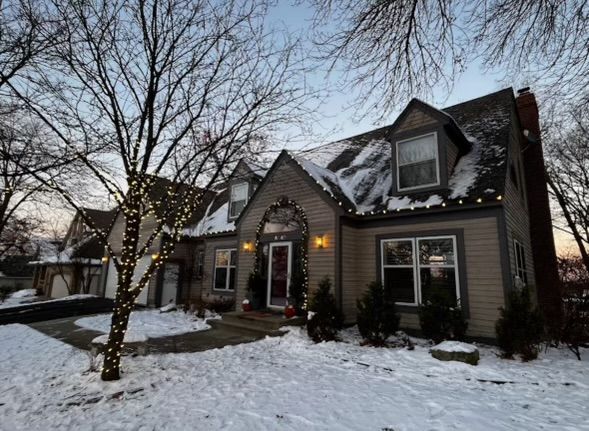 A house with Christmas lights on the roof is covered in snow.