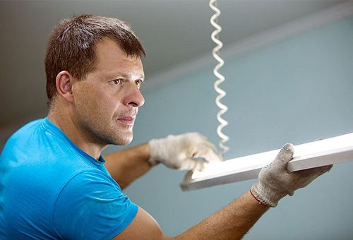 Electrician man worker installing ceiling fluorescent lamp