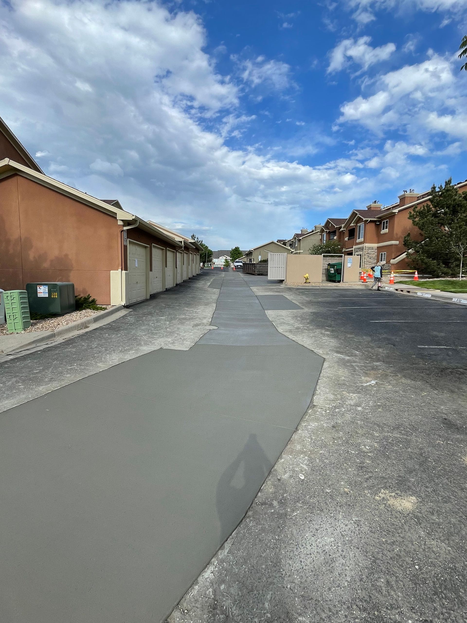 Street resurfacing in a residential area. Freshly paved grey asphalt contrasts with older, gravel-like pavement under a blue sky.