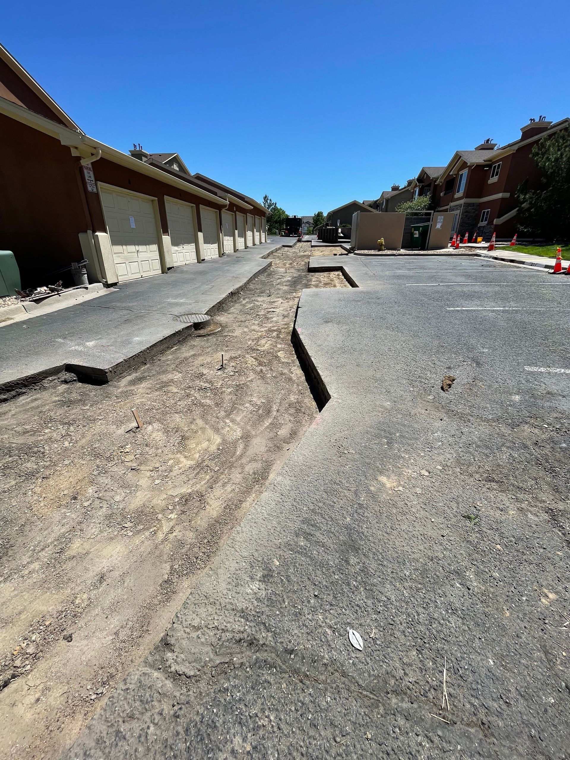 Damaged asphalt road during construction, with exposed dirt and building facades flanking it.