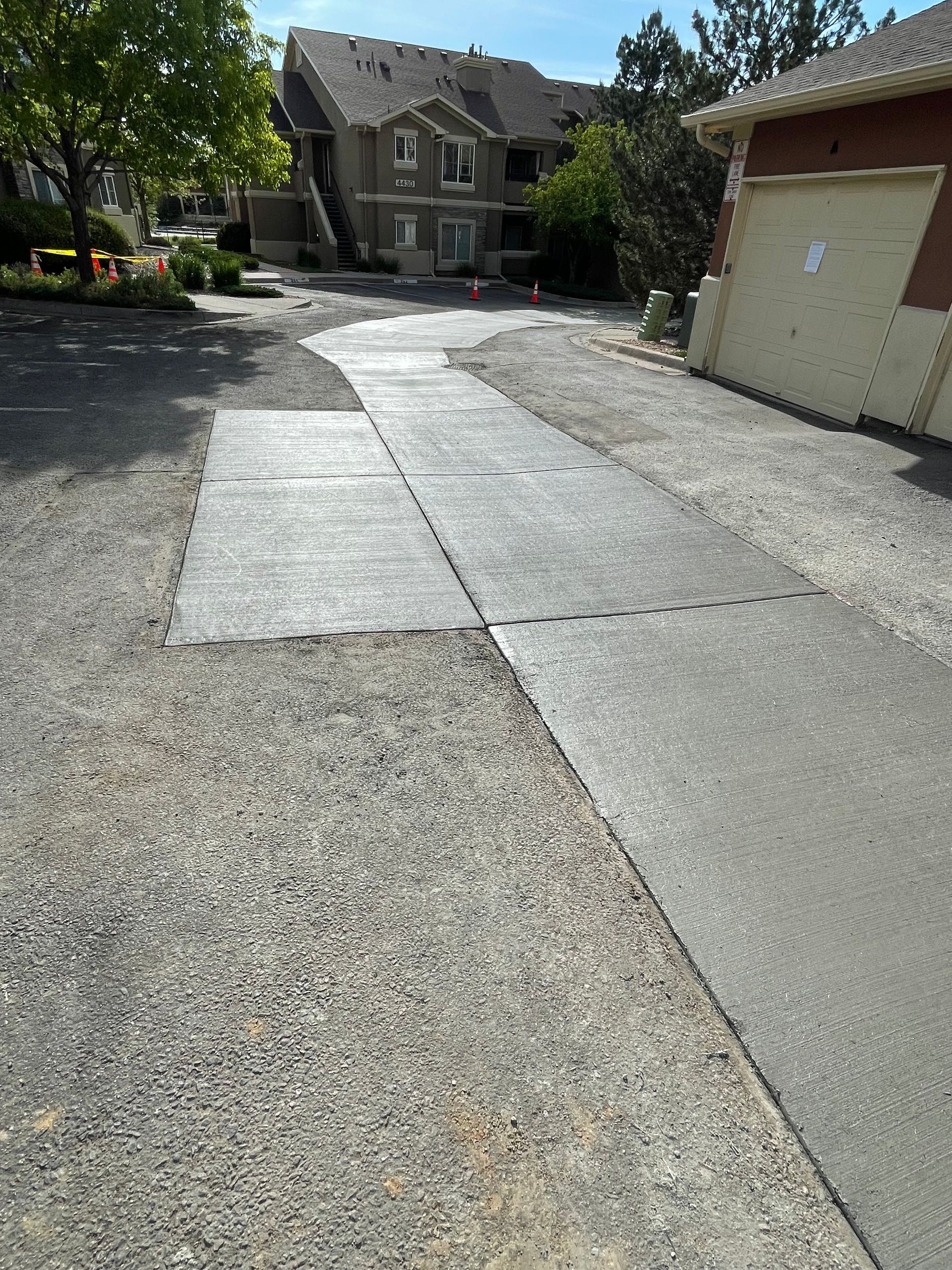 Driveway with patched asphalt and gravel edges, leading to a building with a garage door.