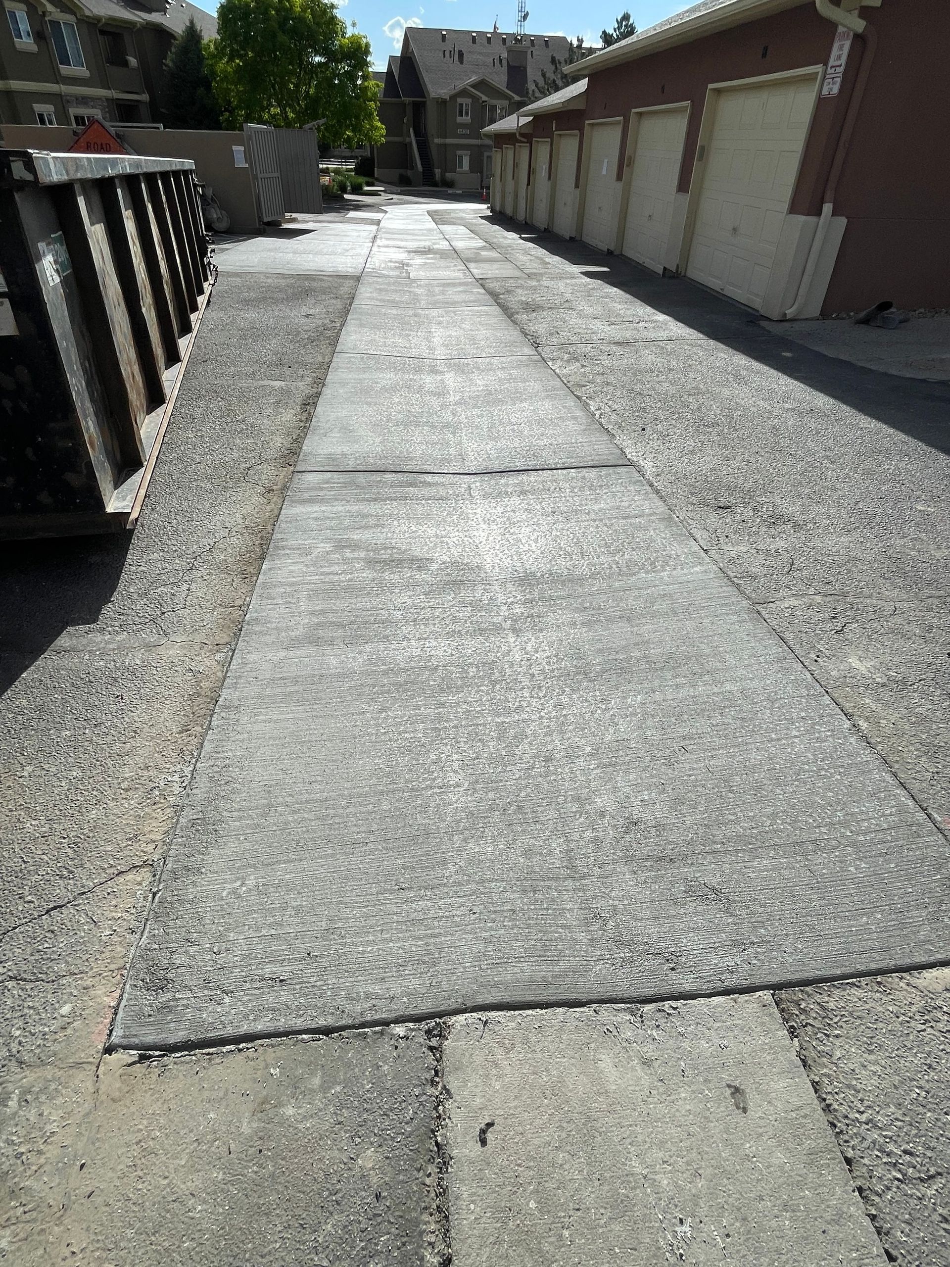 Concrete alleyway lined with gravel, buildings, and dumpsters. The center has a worn concrete slab.