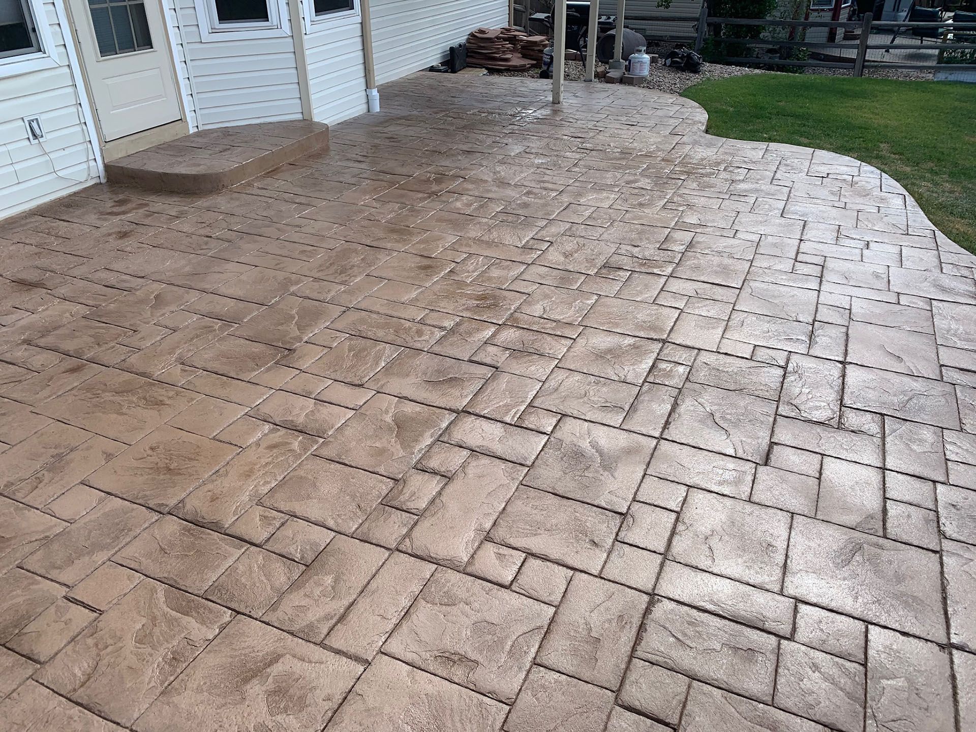A patio with a brick pattern and steps leading to a house.
