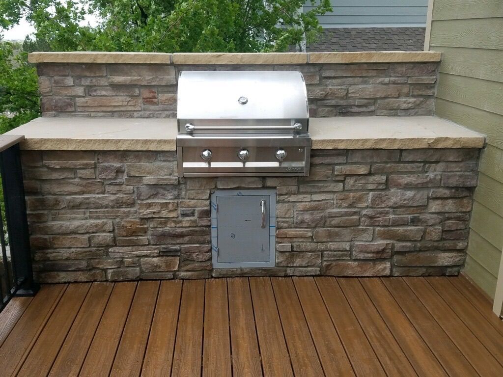 A grill is built into a stone wall on a deck