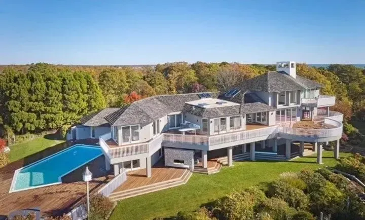 Large gray multi-level house with a pool, decks, and a green lawn.