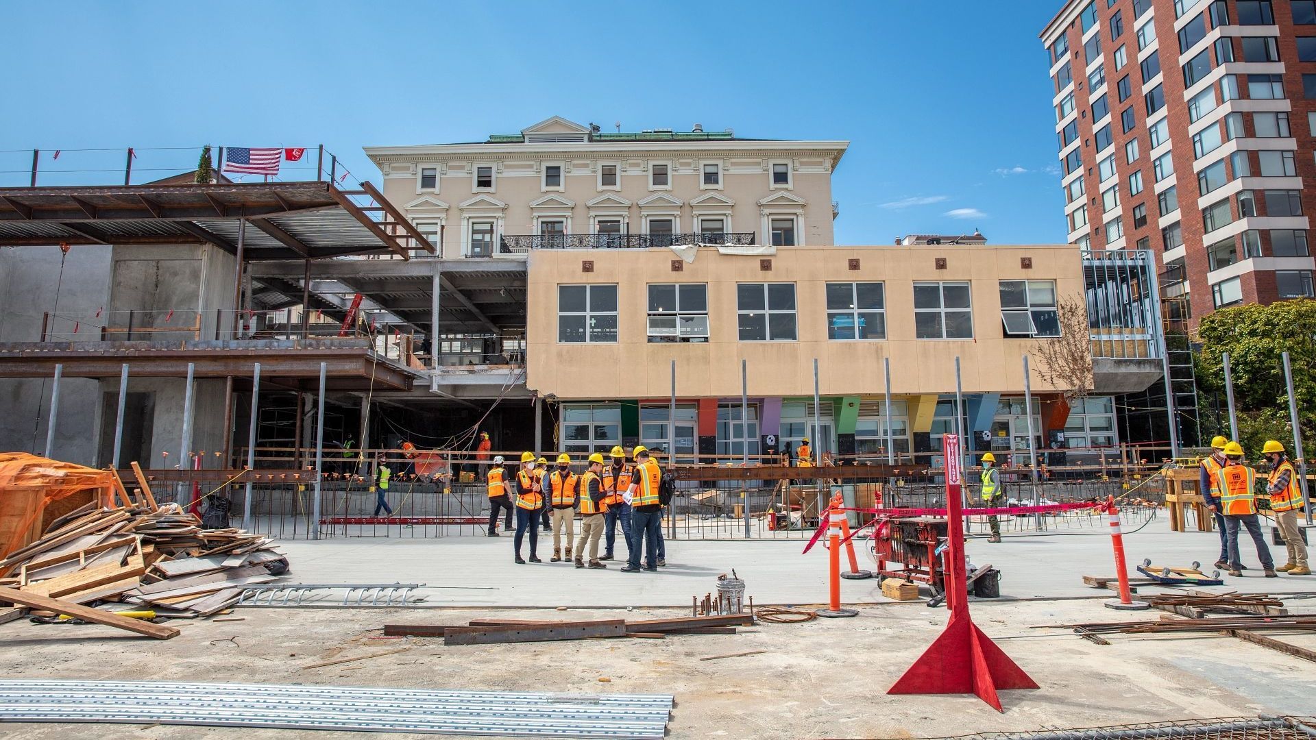Construction workers in orange vests on a building site with scaffolding and a partially built structure under blue sky