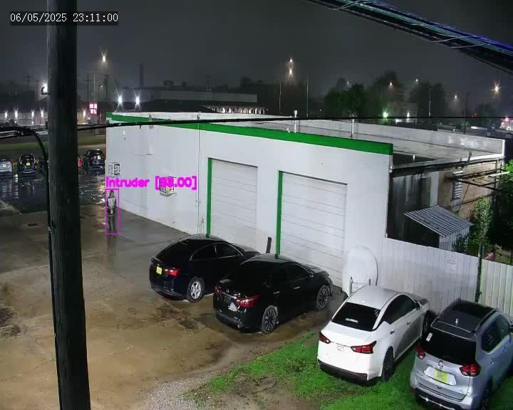 Nighttime parking lot beside a white garage, with four parked cars and a fence identifying an intruder on the security camera footage.
