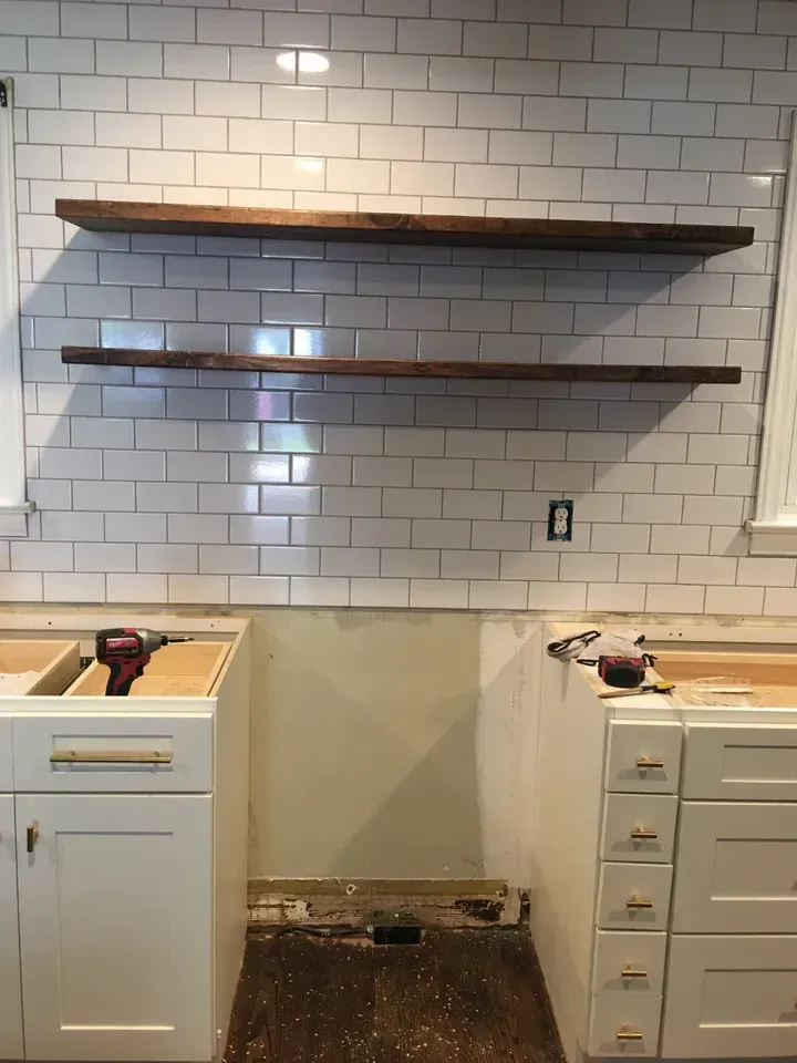 A kitchen with white cabinets and wooden shelves.