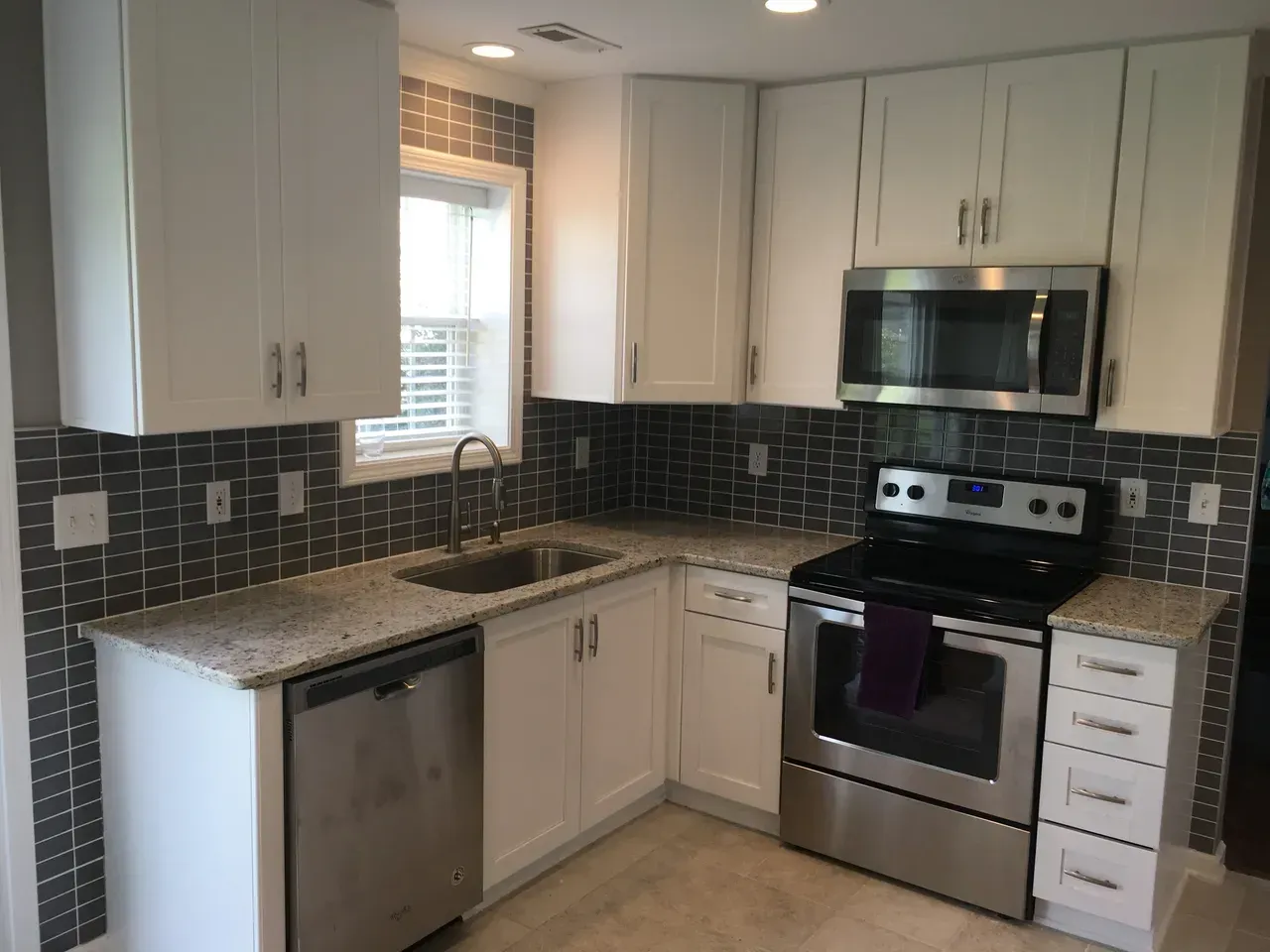 A kitchen with white cabinets , stainless steel appliances , a sink , and a window.