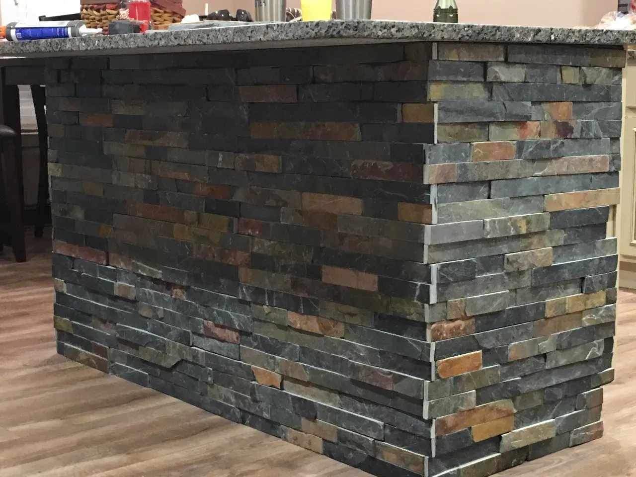 A kitchen island with a brick wall and granite counter top.