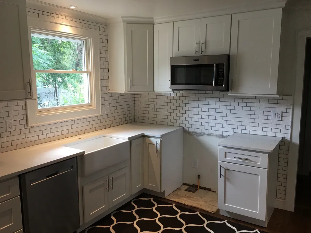 A kitchen with white cabinets , stainless steel appliances , a microwave and a window.