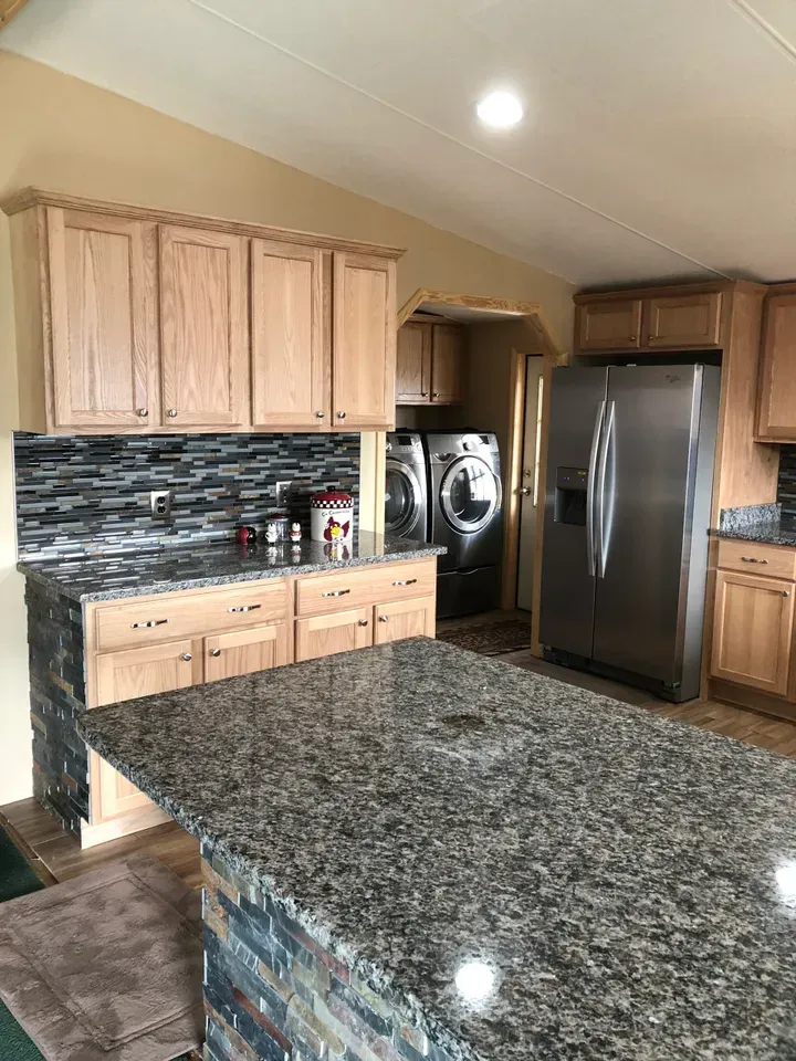 A kitchen with wooden cabinets , granite counter tops , and a stainless steel refrigerator.