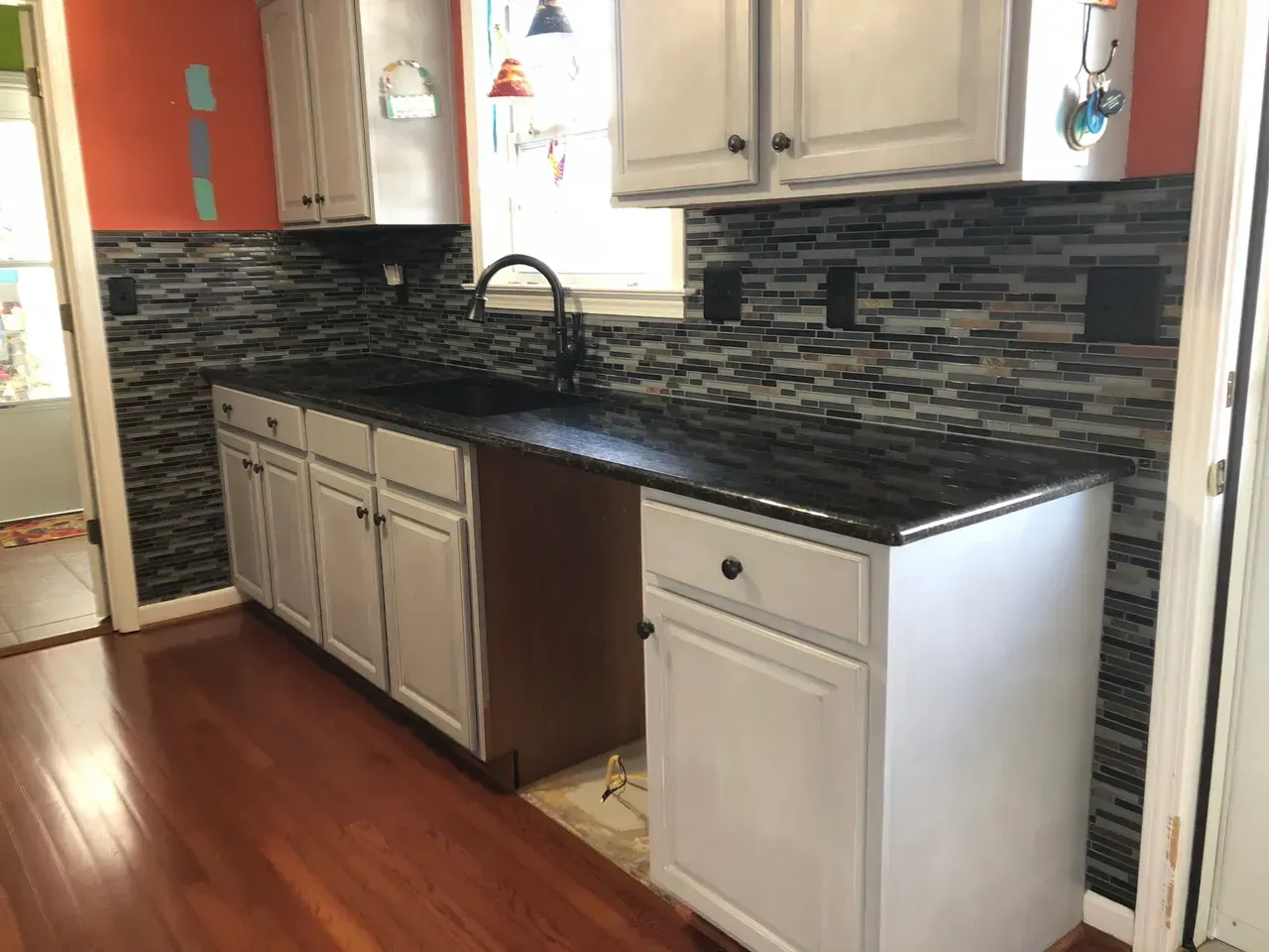 A kitchen with white cabinets , black counter tops , and a sink.