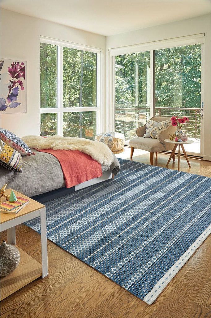 A bedroom with a bed , chair , table and blue rug.