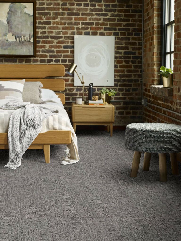 A bedroom with a bed , nightstand , stool and a brick wall.