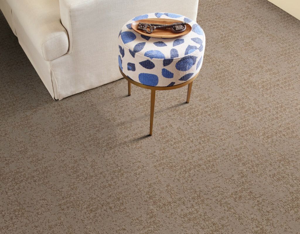 A blue and white ottoman is sitting on a carpeted floor next to a couch.