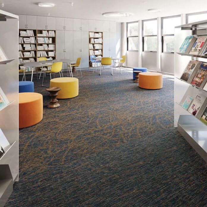 A library with tables , chairs , ottomans and bookshelves.