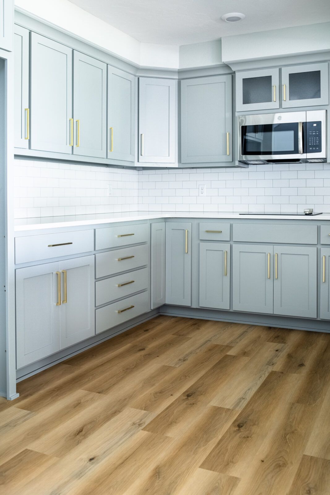 A kitchen with white cabinets , wooden floors , and a microwave.