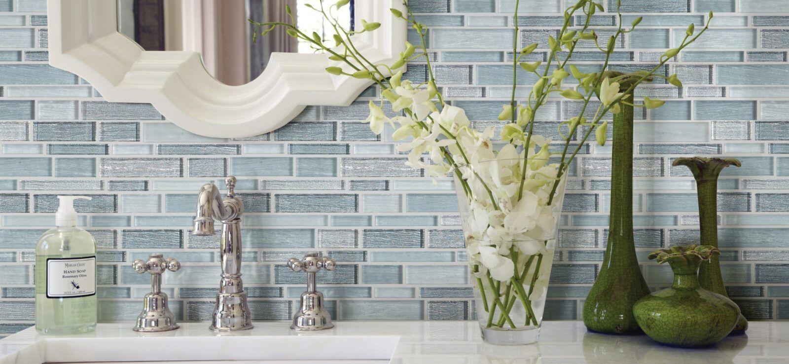 A bathroom with a sink , mirror , vases and flowers.