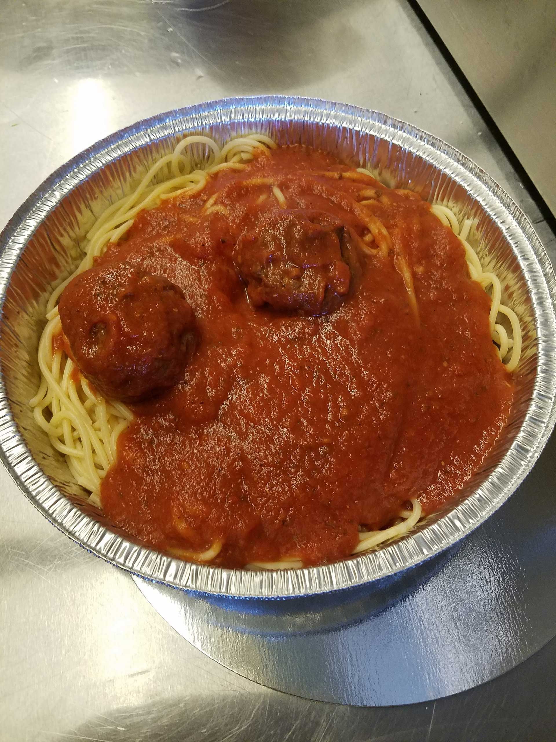 spaghetti and meatballs in a foil container, covered in red sauce