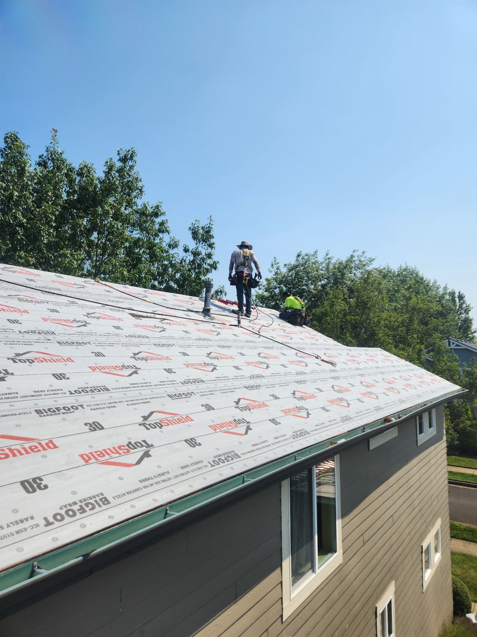 Roofers installing roofing material on a house, under a sunny blue sky.