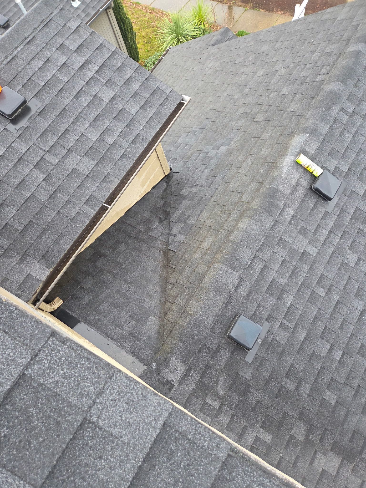 Overhead view of a gray shingle roof with a tan-colored wooden structure angled upwards.