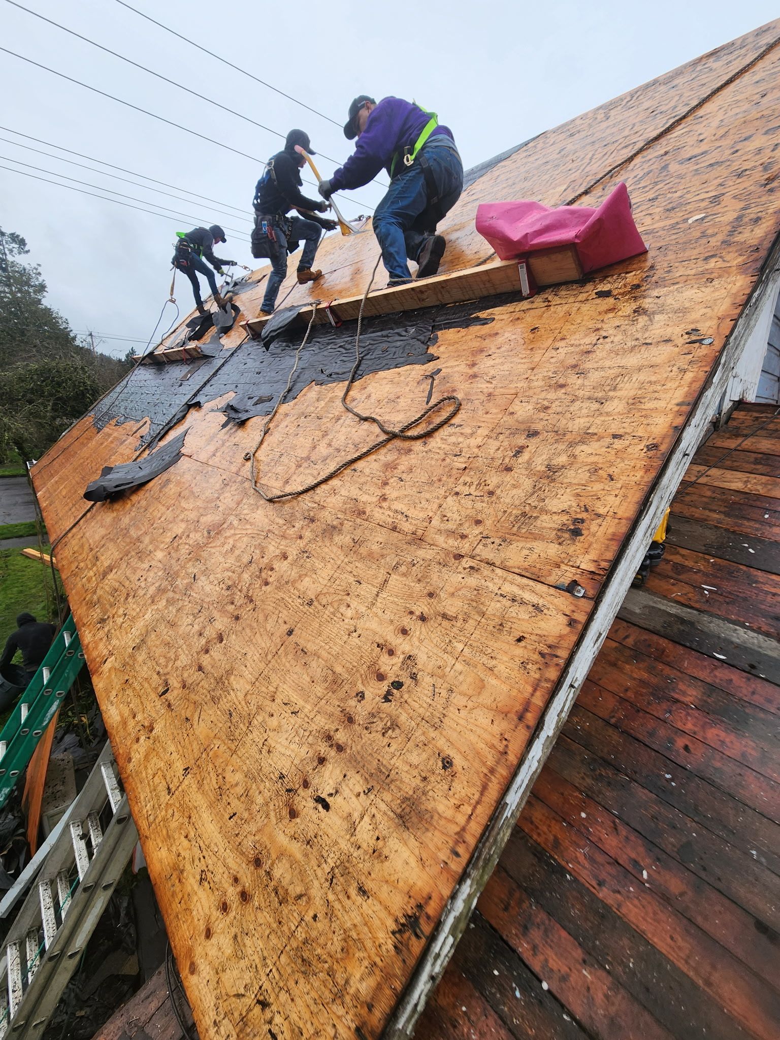 Roofers working on a partially shingled roof under an overcast sky.
