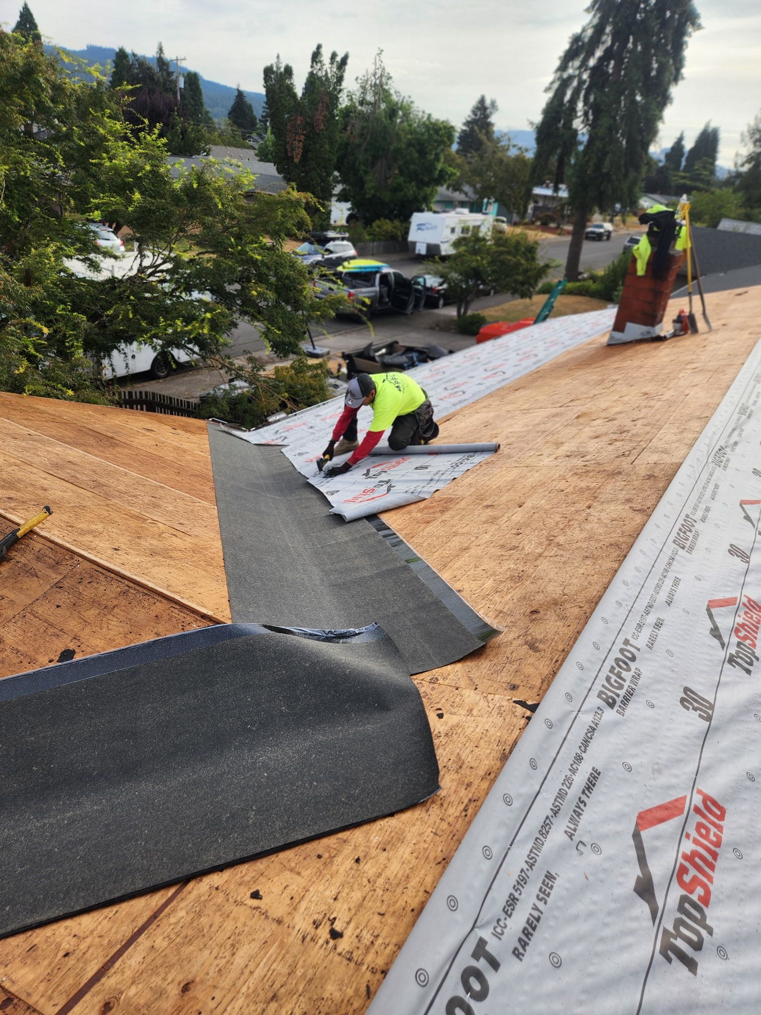 Roofers installing roofing material on a house; one cutting the material, another standing nearby.