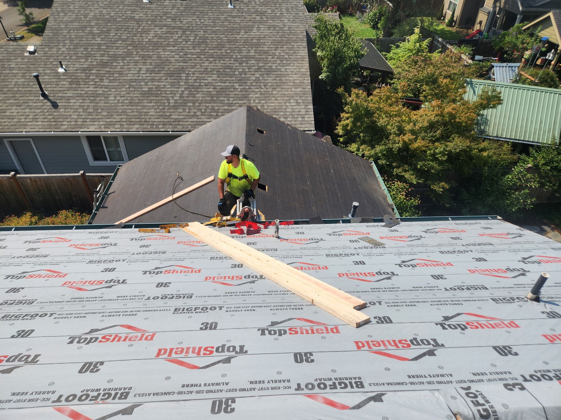 Roofer on a roof, installing materials. Roof is covered in black underlayment; other roofs are visible in background.
