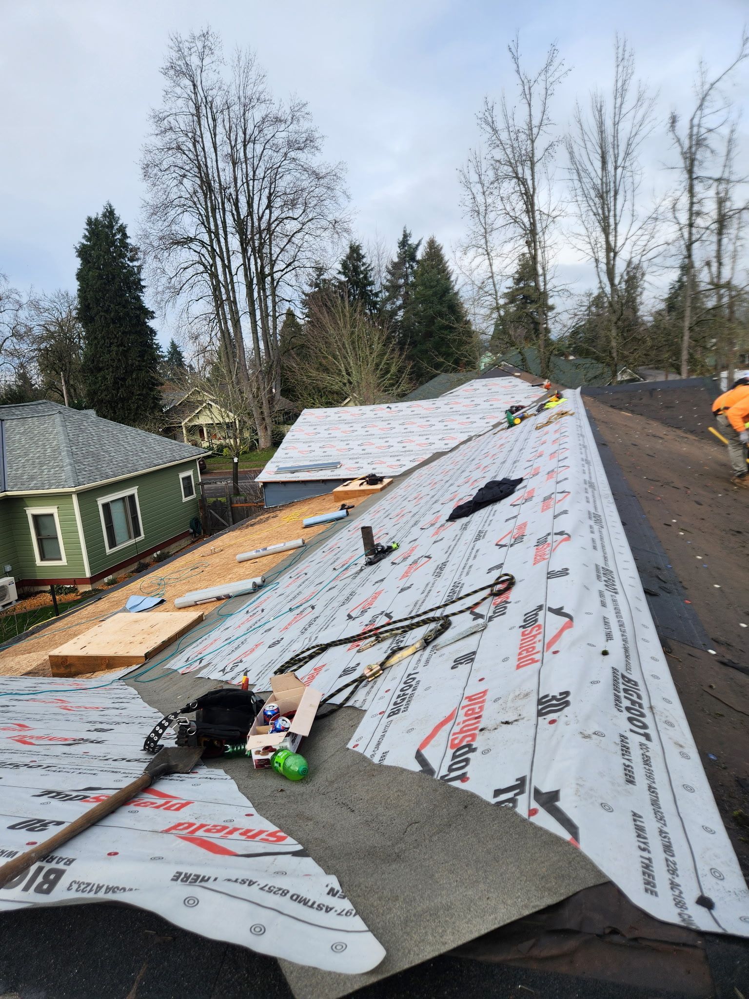 Roof being worked on, with underlayment and partially installed shingles. Trees and houses in background.