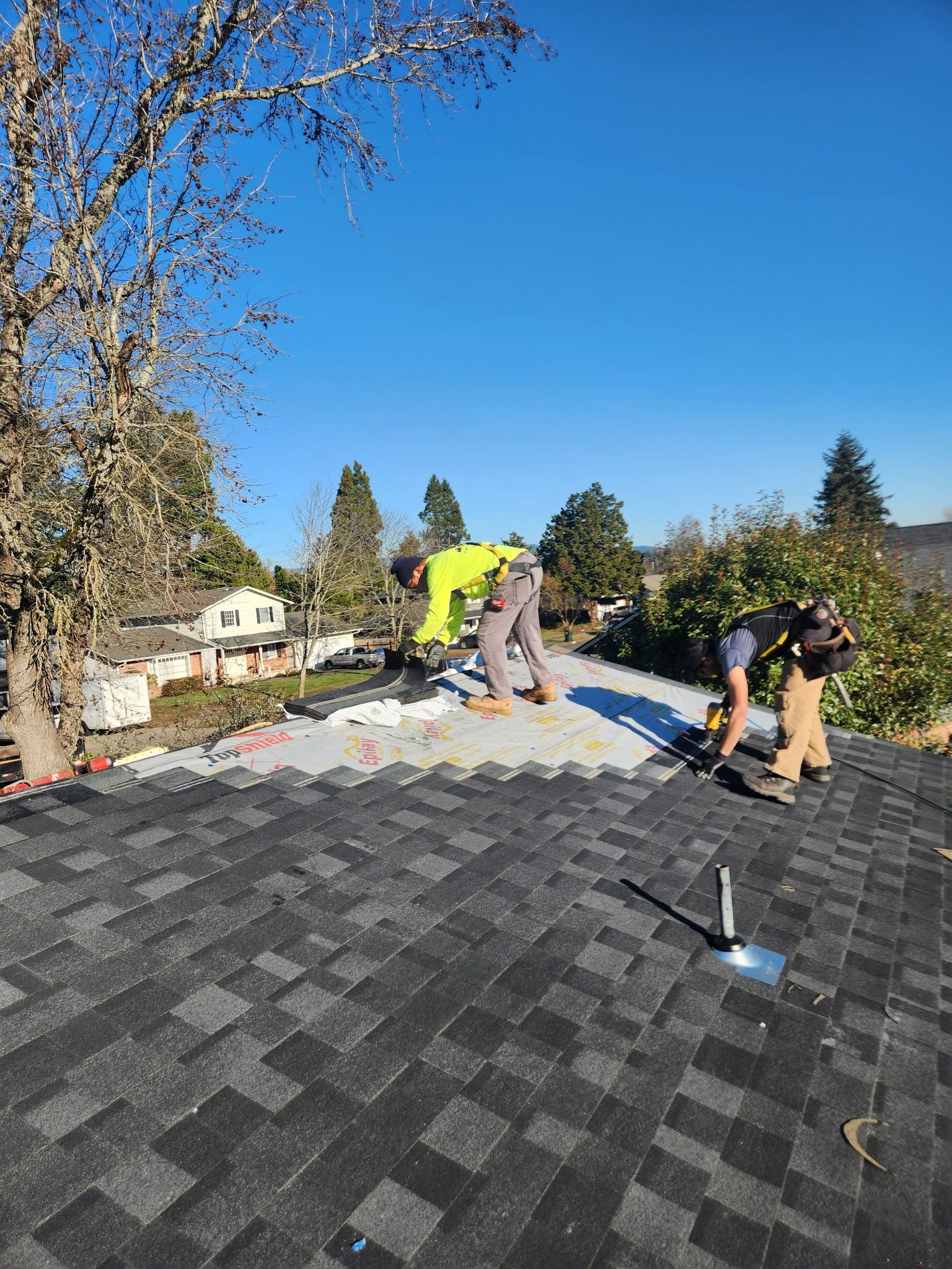 Two roofers installing new shingles on a house roof on a sunny day.