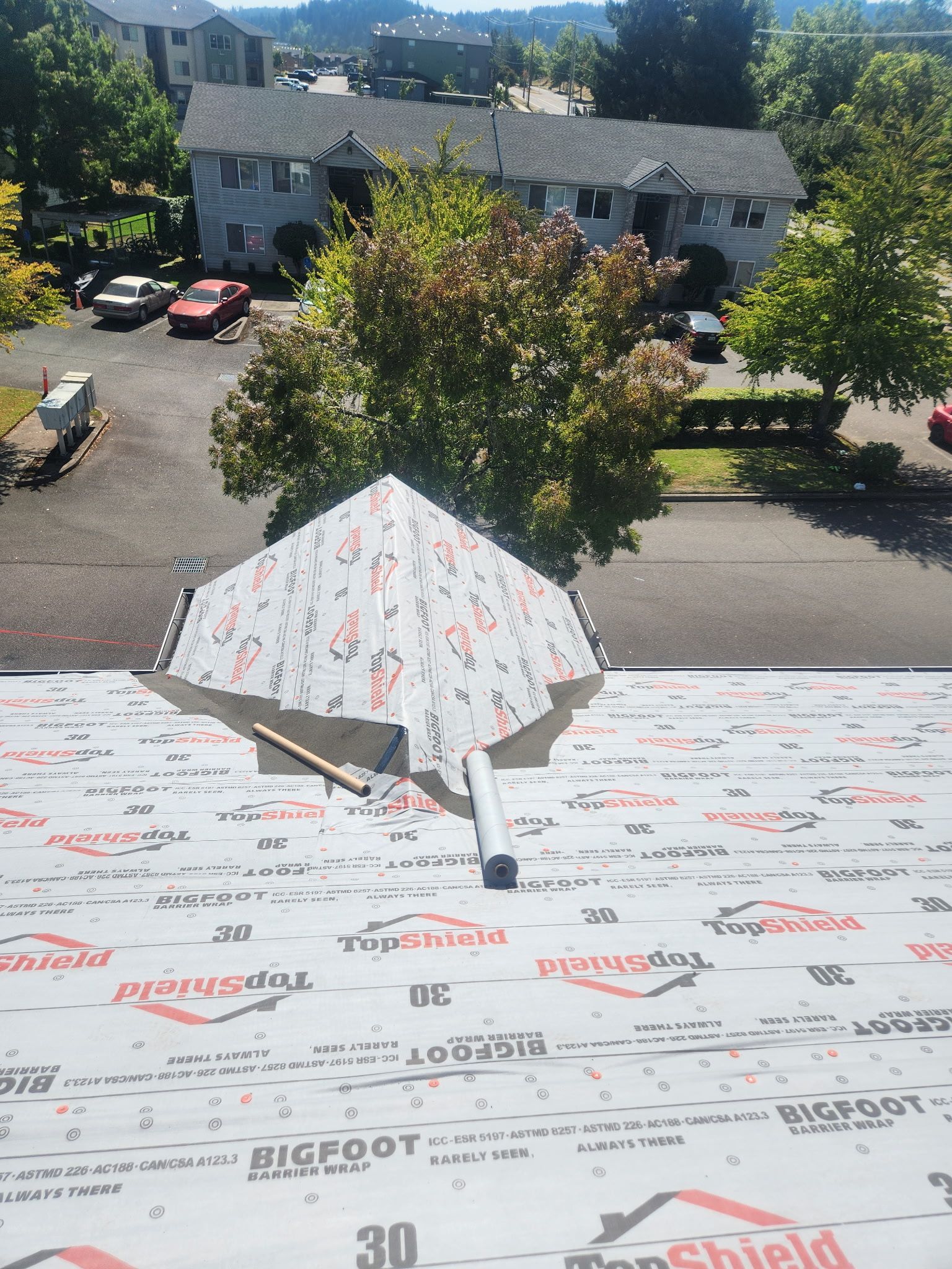 Rooftop with white/red/black material, pipe, and a partially covered structure; background of a neighborhood with trees and cars.