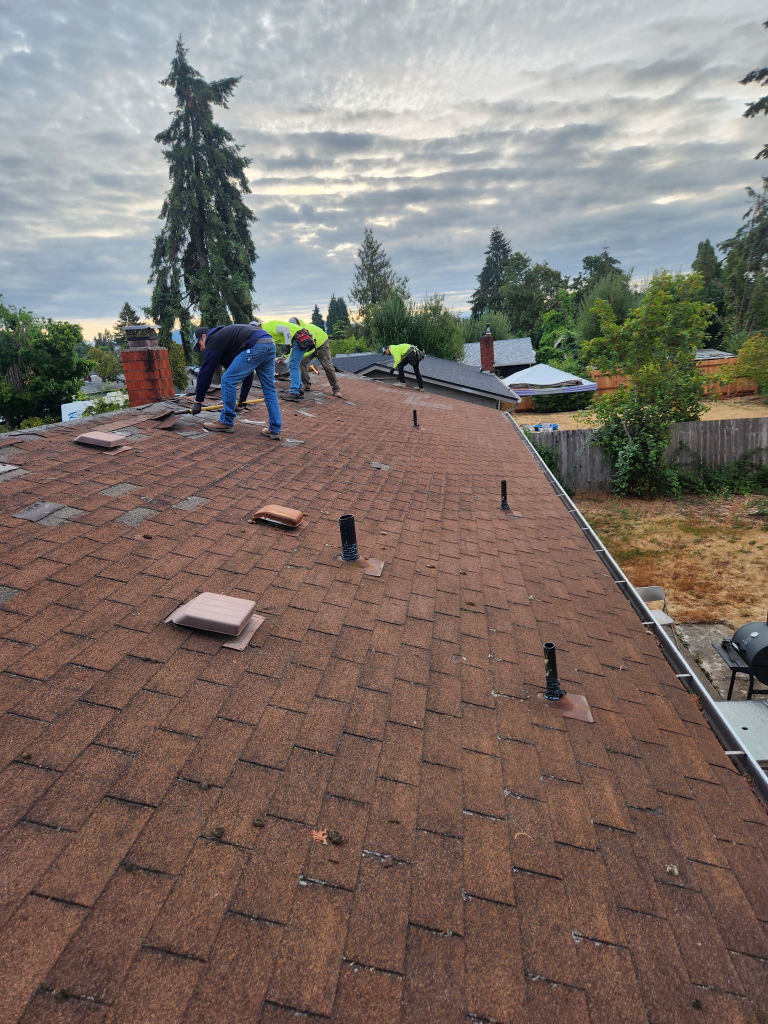 Roofers working on a brown shingle roof, cloudy sky overhead.