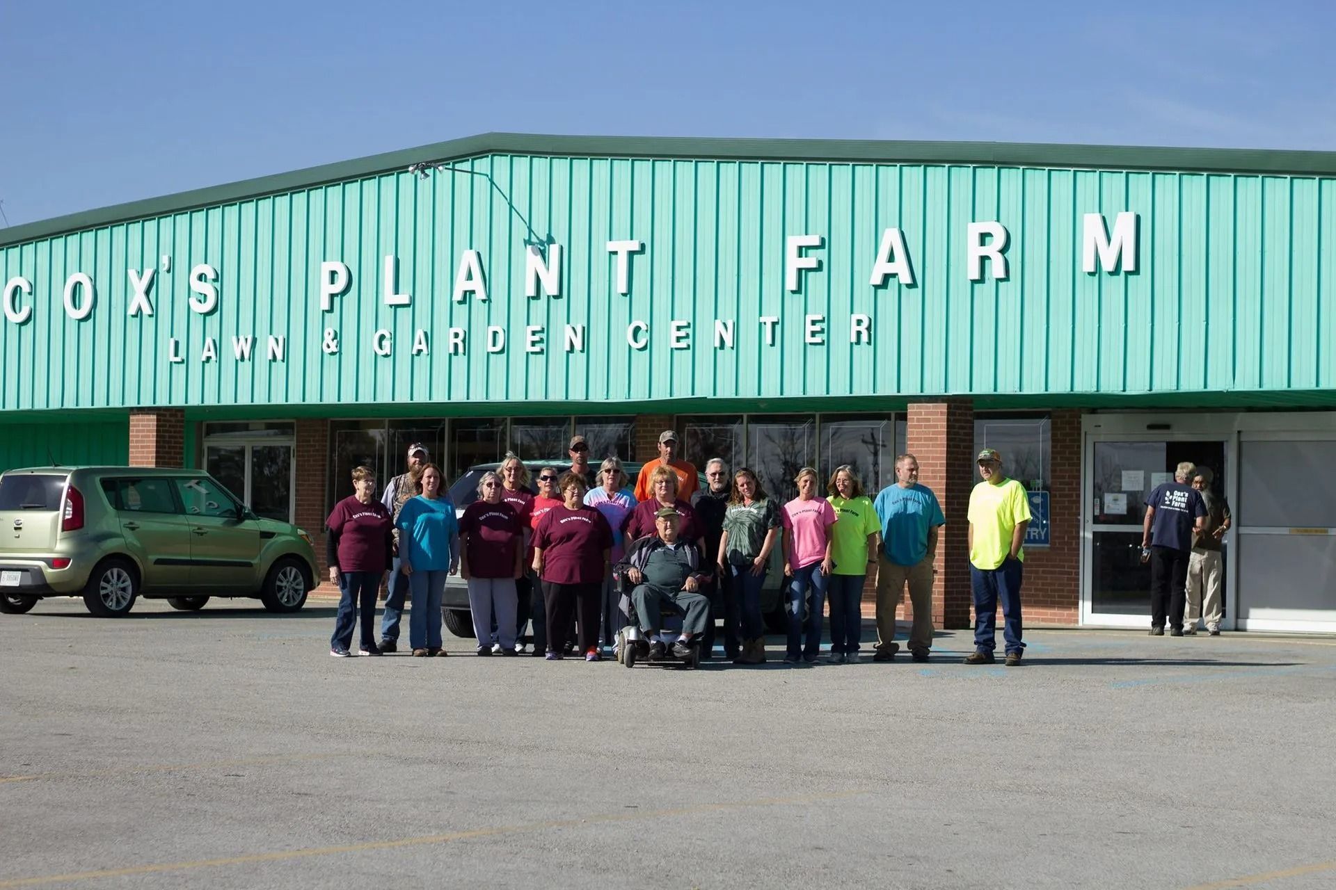 Group of people standing in front of Cox's Plant Farm building. Green building with white letters.