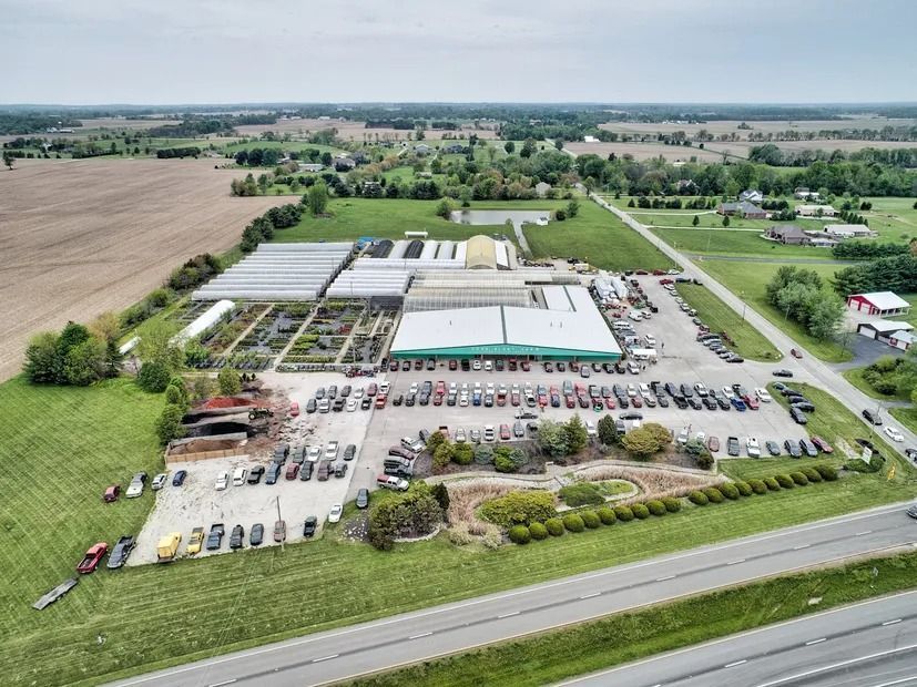 Aerial view of a garden center with greenhouses, retail buildings, and a parking lot next to a highway.