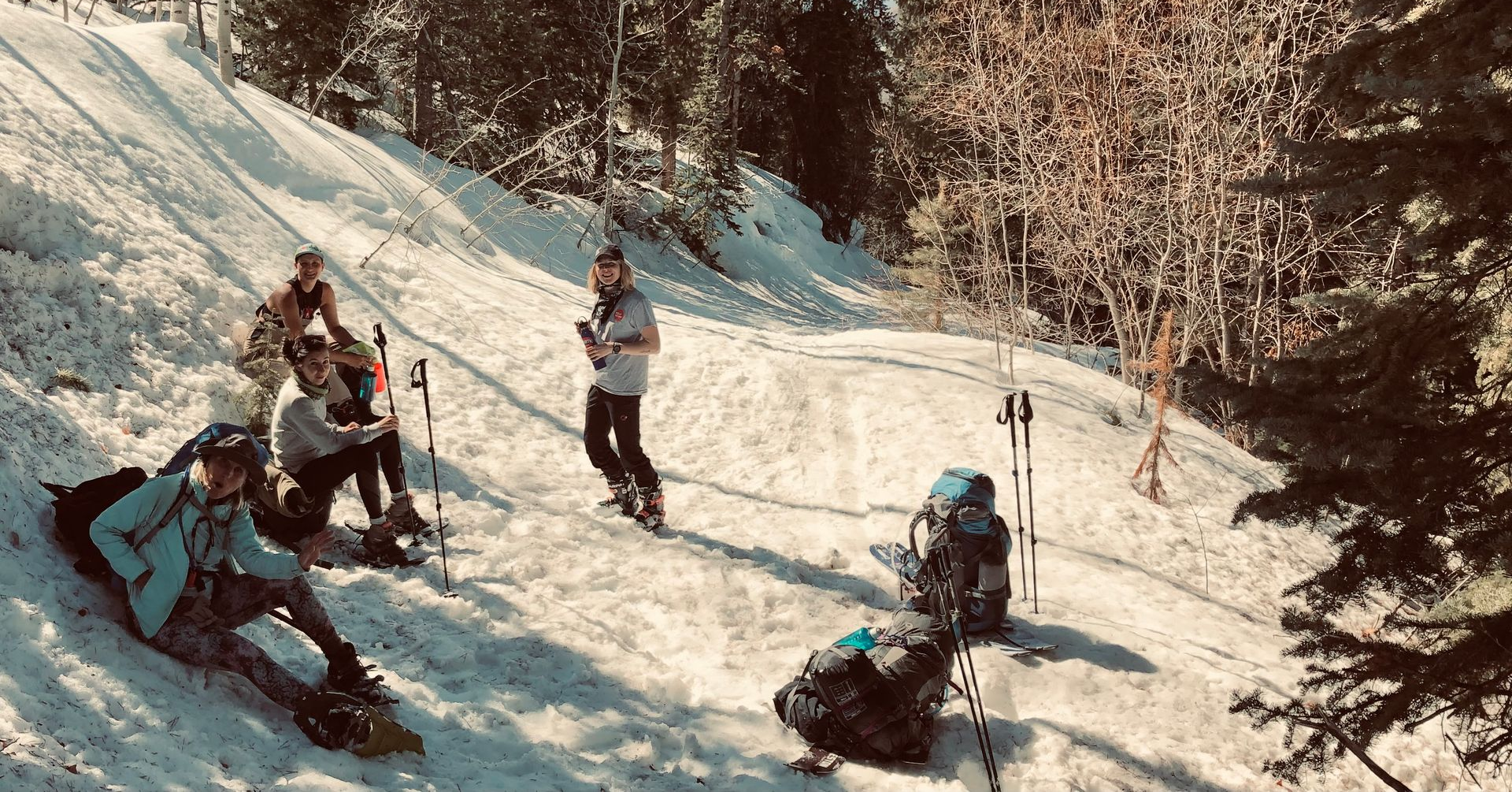 Man doing a revolved prayer twist yoga pose outdoors with a bonsai tree in the background before a wooden wall.