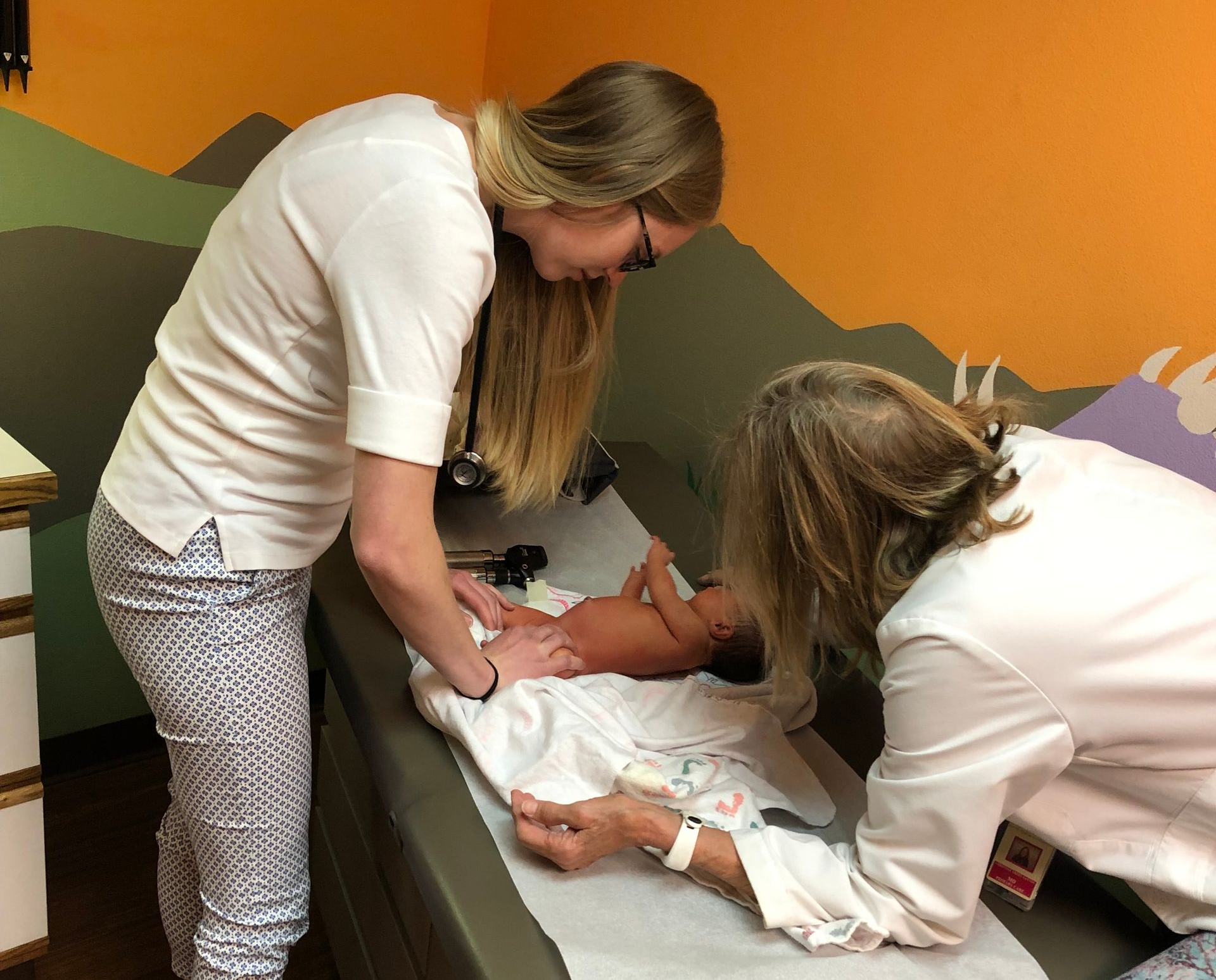 A doctor examines a man's bandaged arm. Doctor wears gloves and a stethoscope.