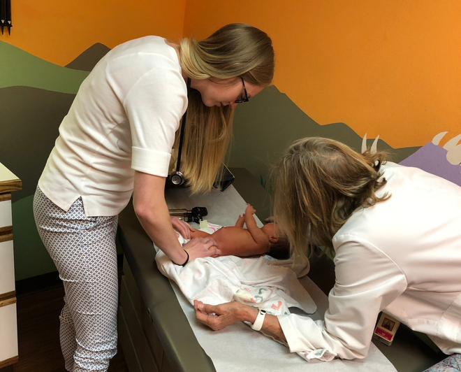 A doctor examines a man's bandaged arm. Doctor wears gloves and a stethoscope.