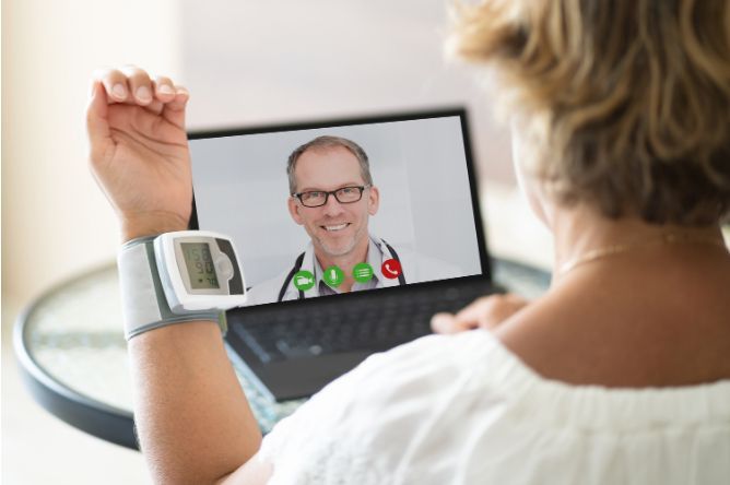 Woman with a blood pressure monitor on her wrist, video-conferencing with a doctor on a laptop