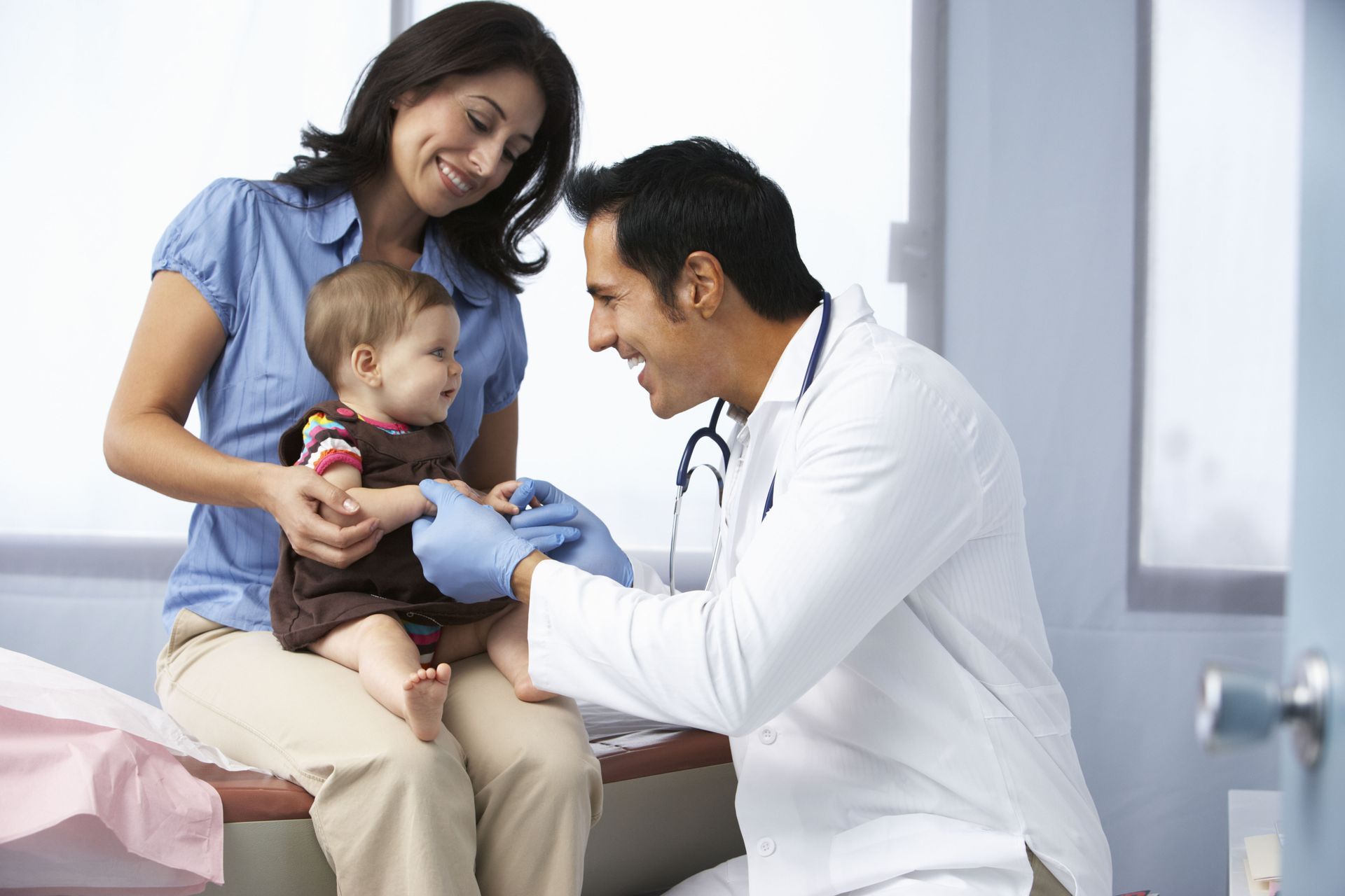 A doctor examines a baby held by a person in a doctor’s office.