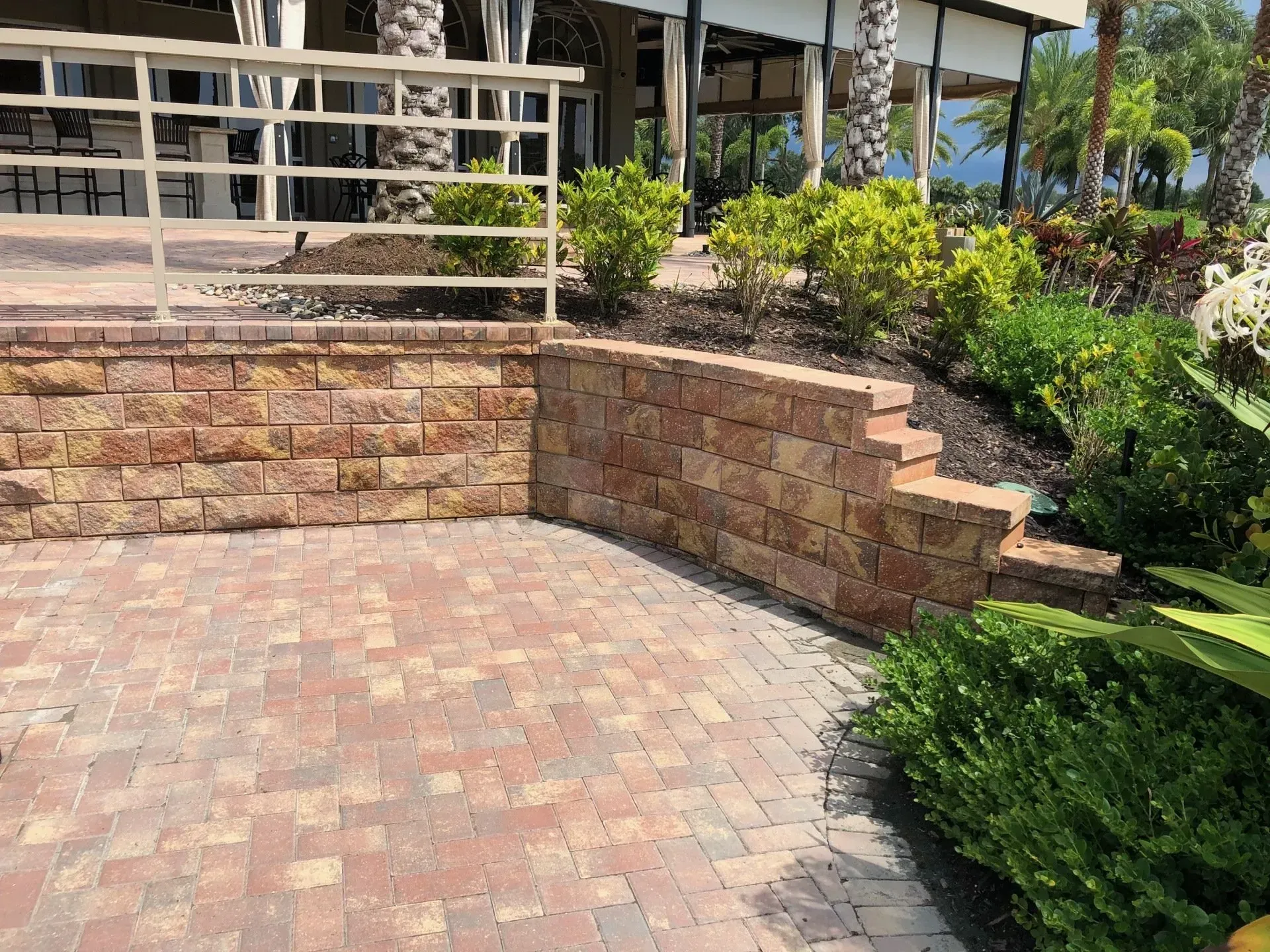 A brick wall is surrounded by plants and a brick walkway.