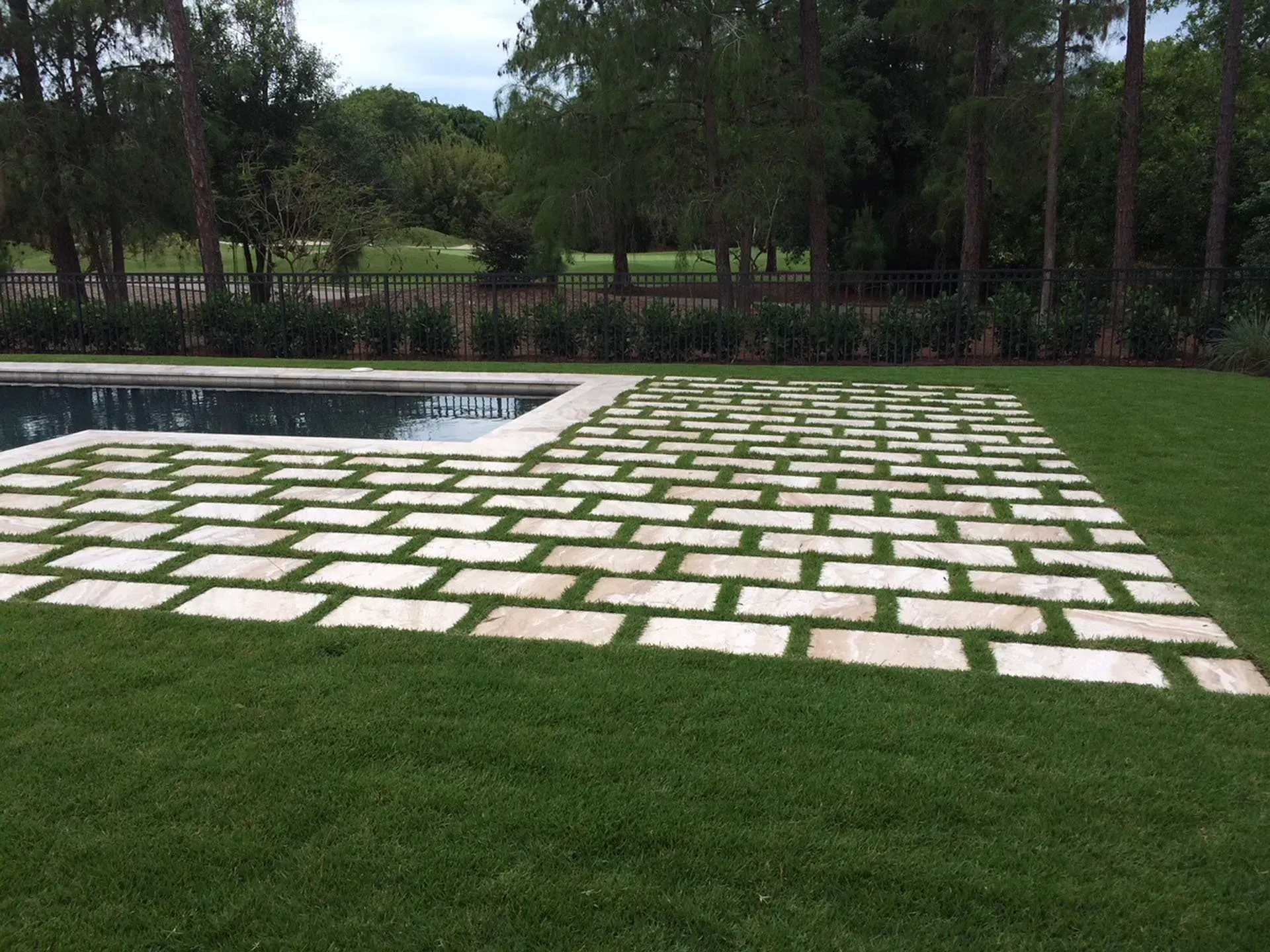 A brick walkway next to a swimming pool in a backyard.