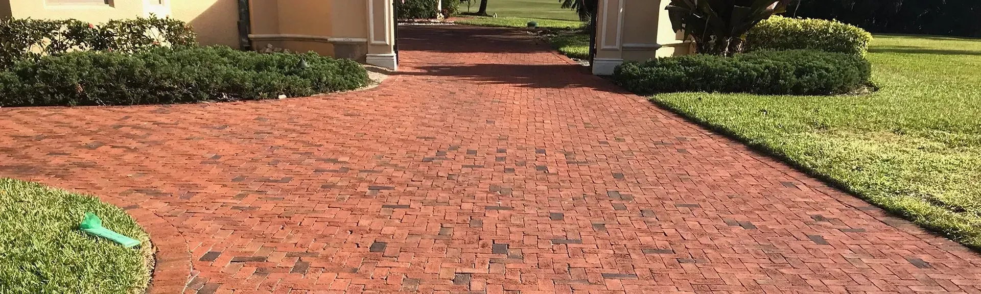 A brick driveway leading to a house with a green hose in the grass.