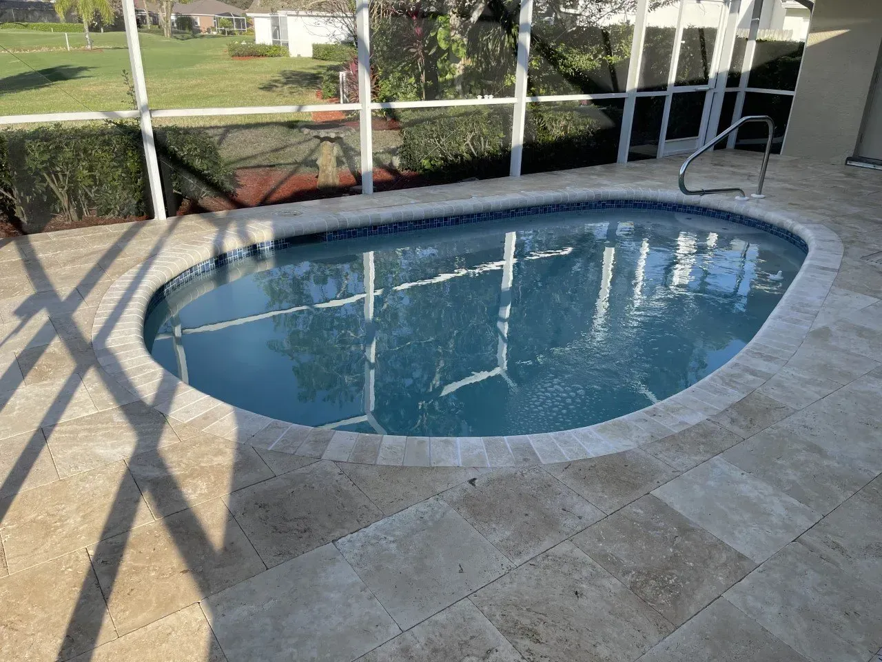 A small oval shaped swimming pool is surrounded by a screened in area