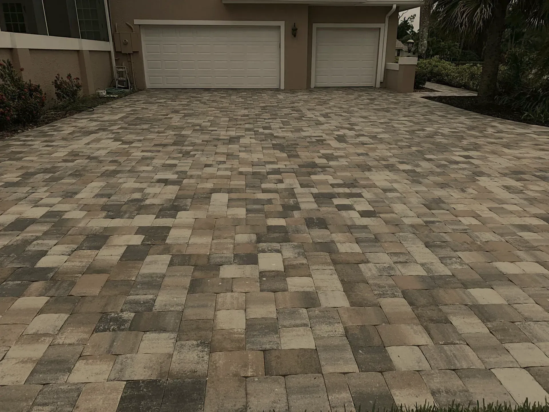A brick driveway in front of a house with two garage doors.