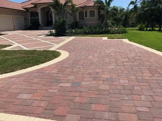 A red brick driveway leading to a large house.